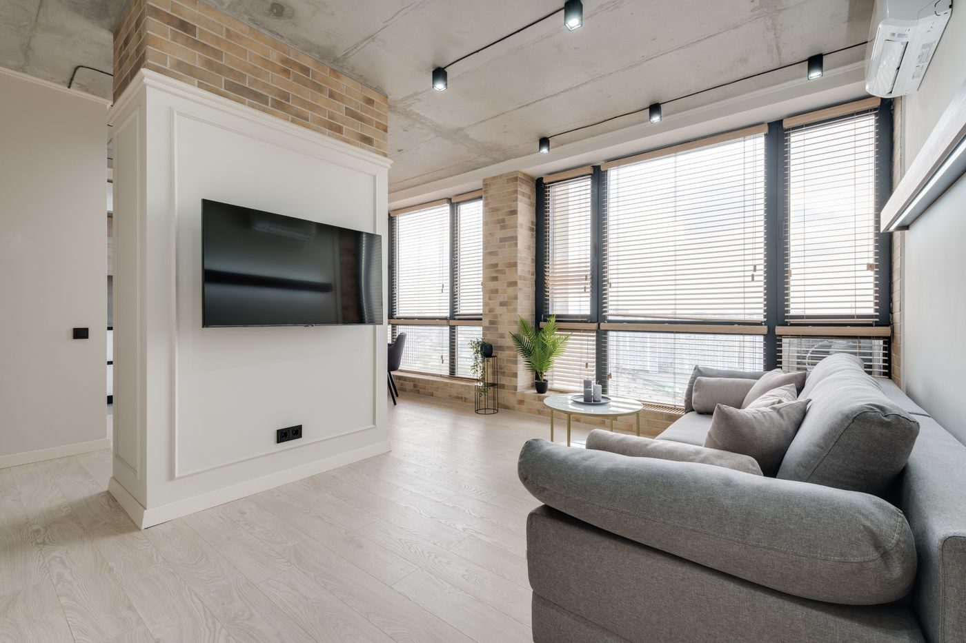 Open plan flat with large windows, exposed brick and a wall mounted air conditioner high on the wall