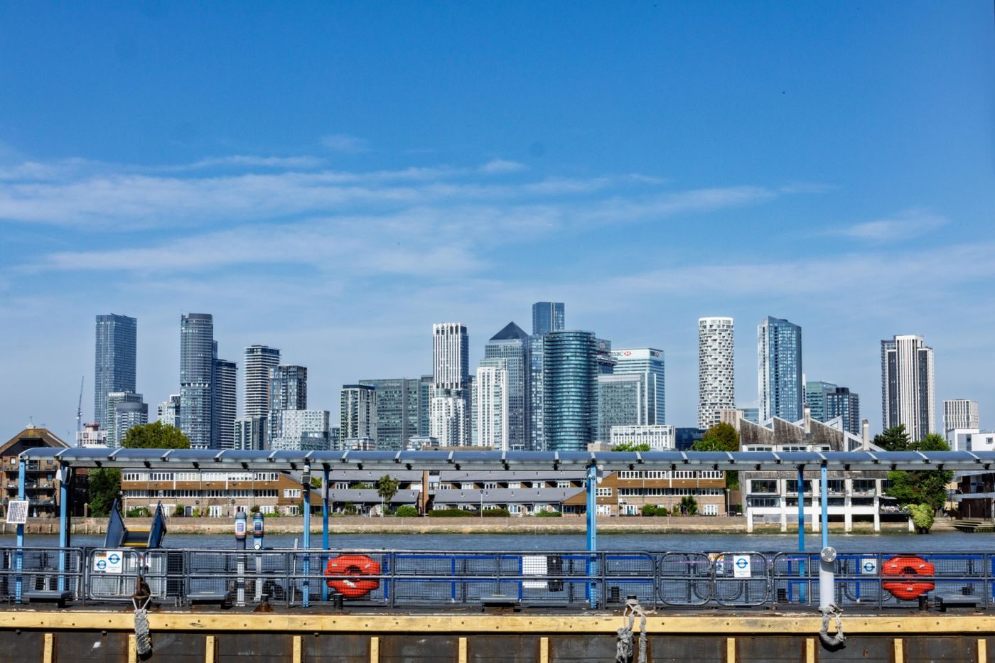 Canary Wharf towers across the River Thames under a clear blue summer sky