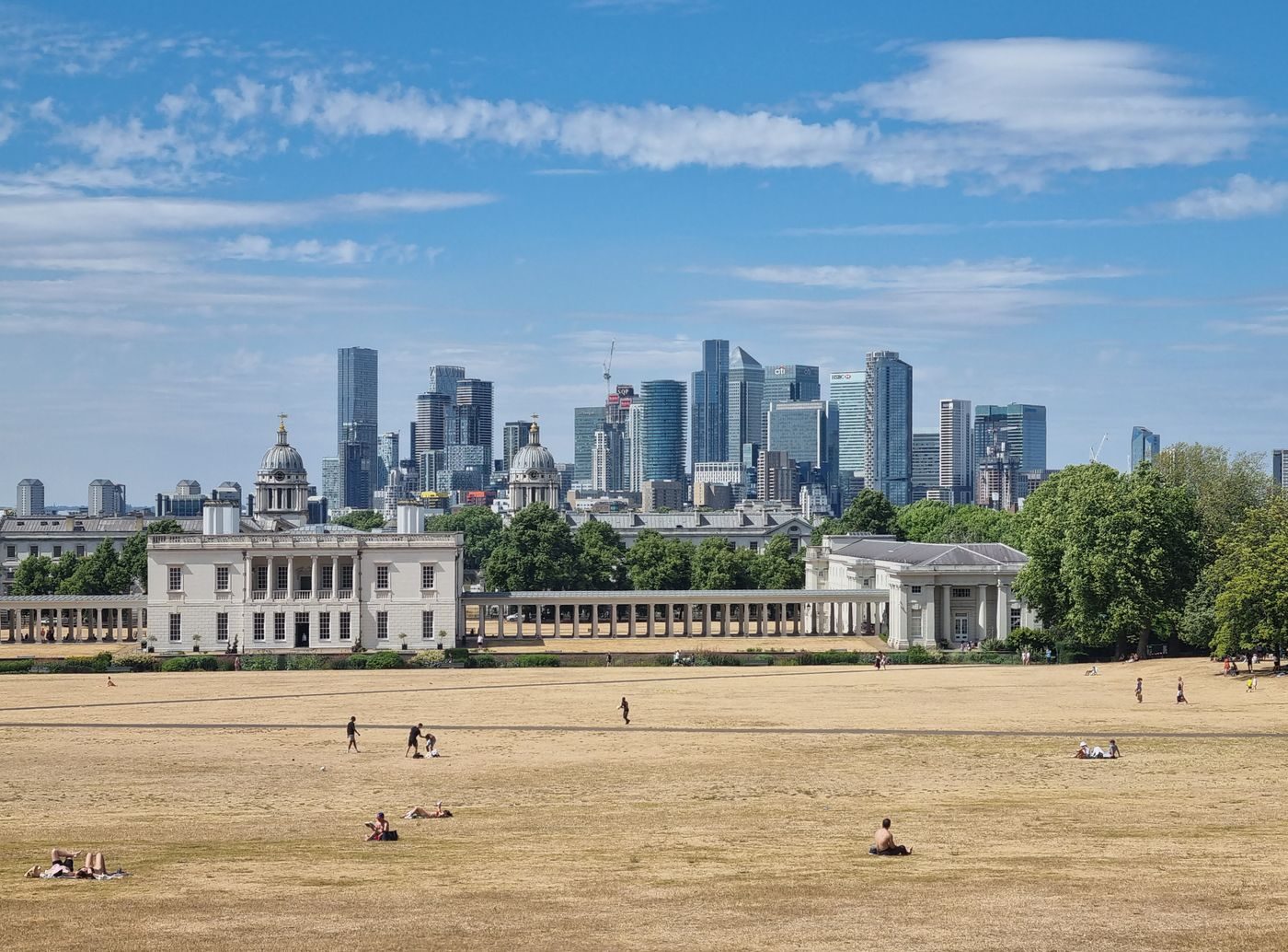 Sun scorched grass in Greenwich Park with the Queen's House and Canary Wharf behind