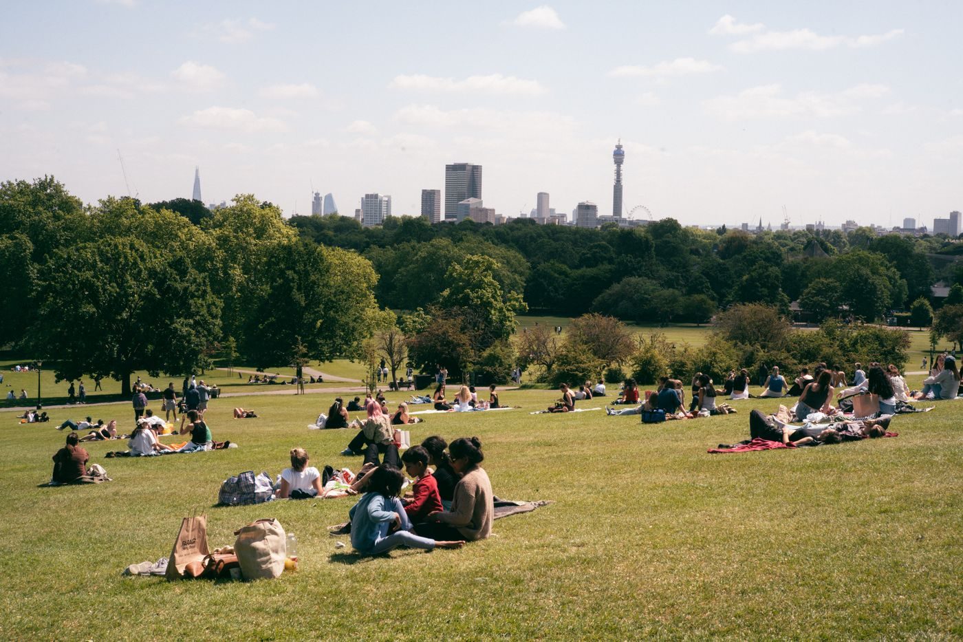 People sitting on the grass on Primrose Hill on a hot day with the London skyline beyond