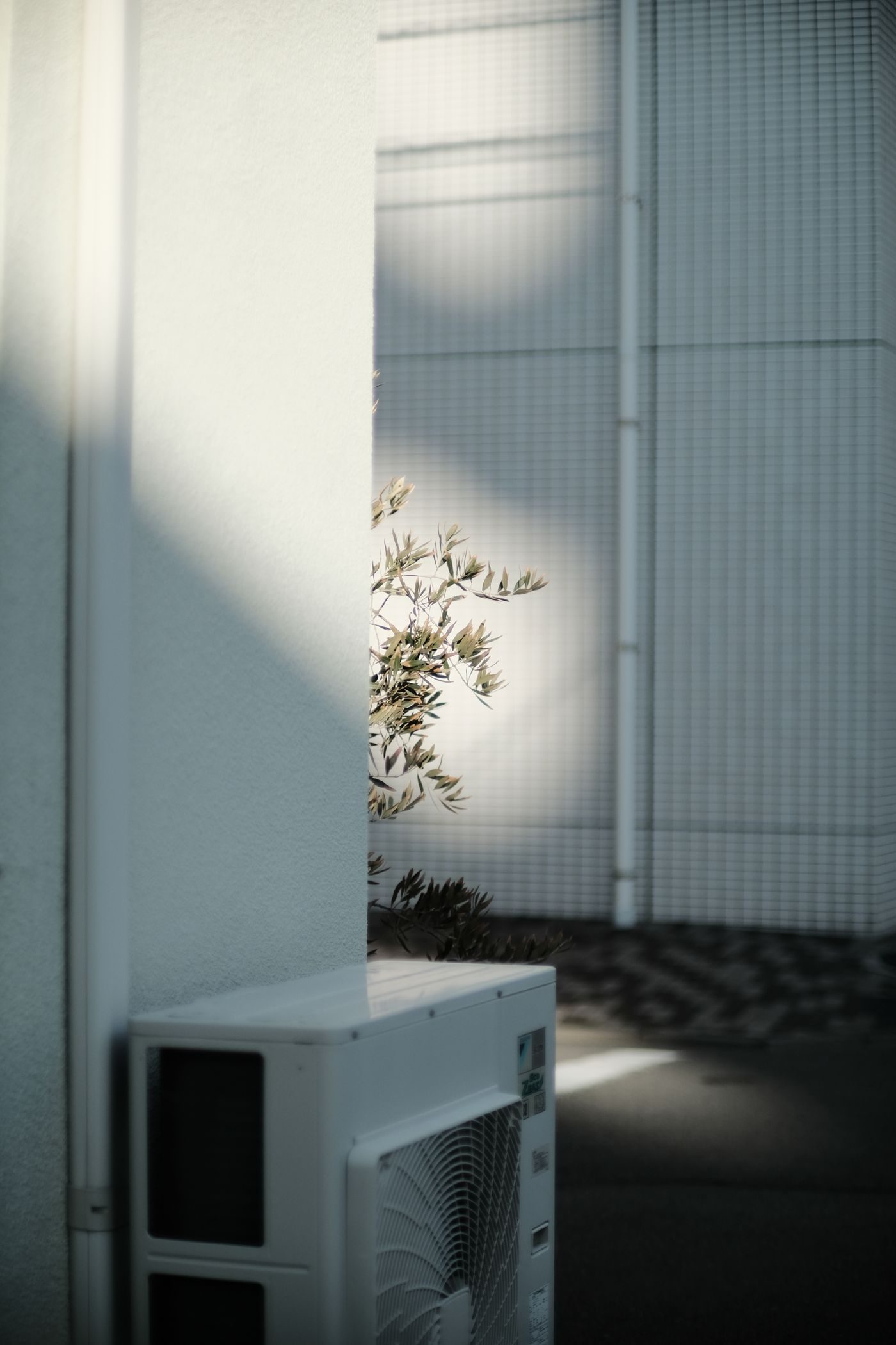 Compact air conditioning outdoor unit sitting against the white wall of a modern building in shade