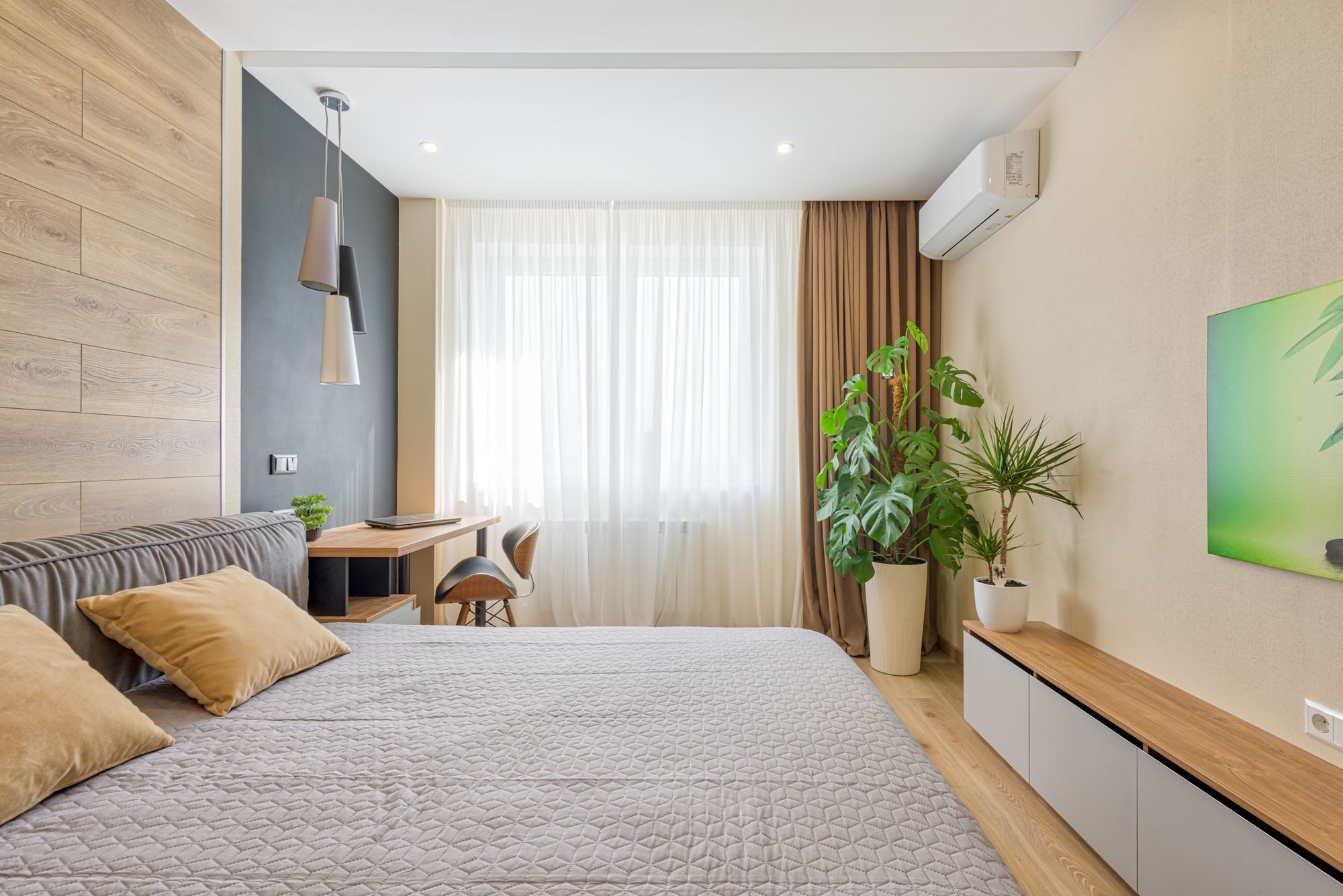 Bright modern bedroom in summer light with a white wall mounted air conditioning unit above the window wall