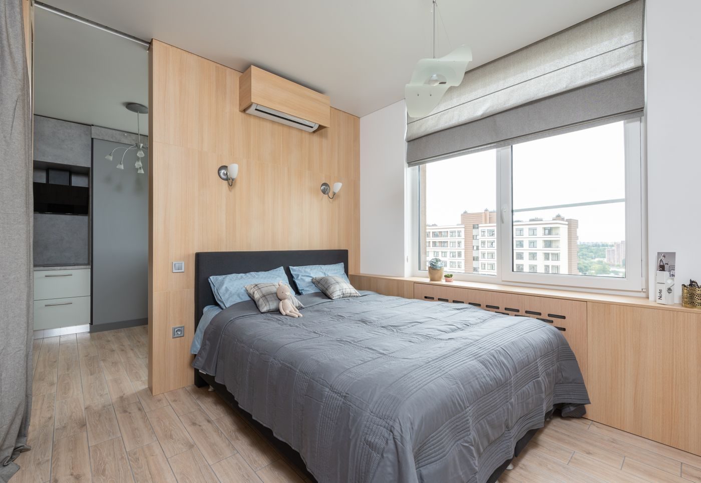 Light bedroom with a white wall mounted air conditioning unit above the bed and a large window